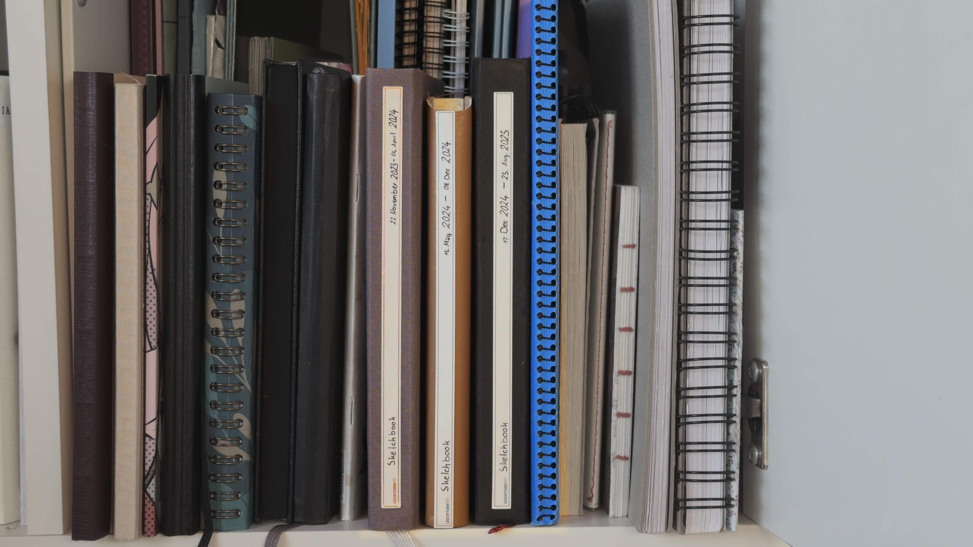 A shelf holding all sketchbooks, spines facing outward.